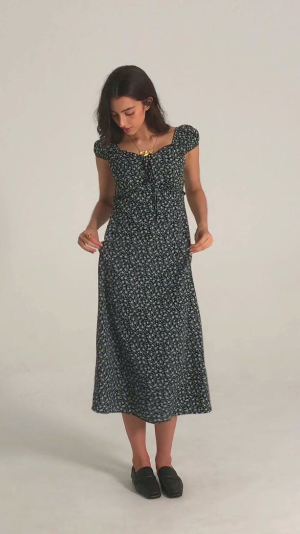 Front view of a woman wearing a black floral midi dress with puff sleeves, ruched bust, and sweetheart neckline