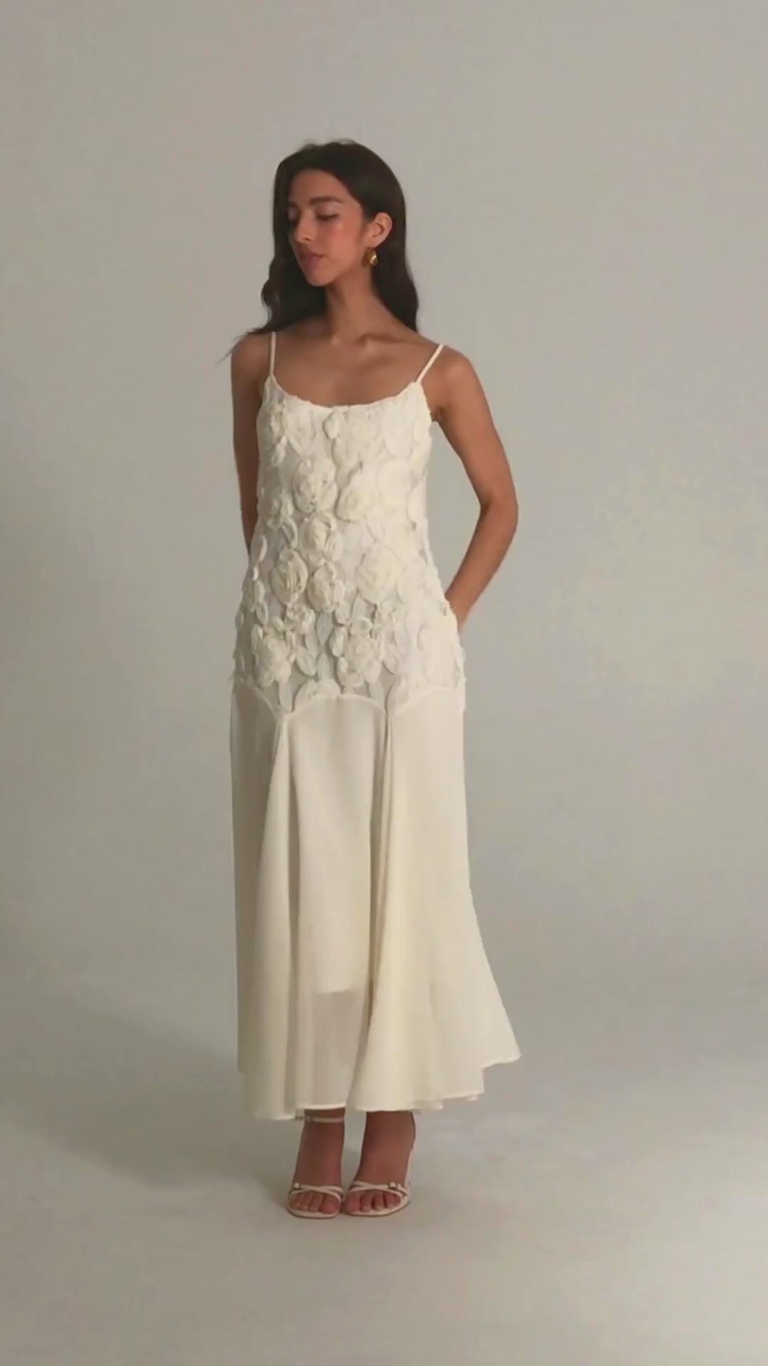 Woman in a white maxi dress featuring 3D floral appliqués and flowy chiffon skirt, styled with delicate spaghetti straps.