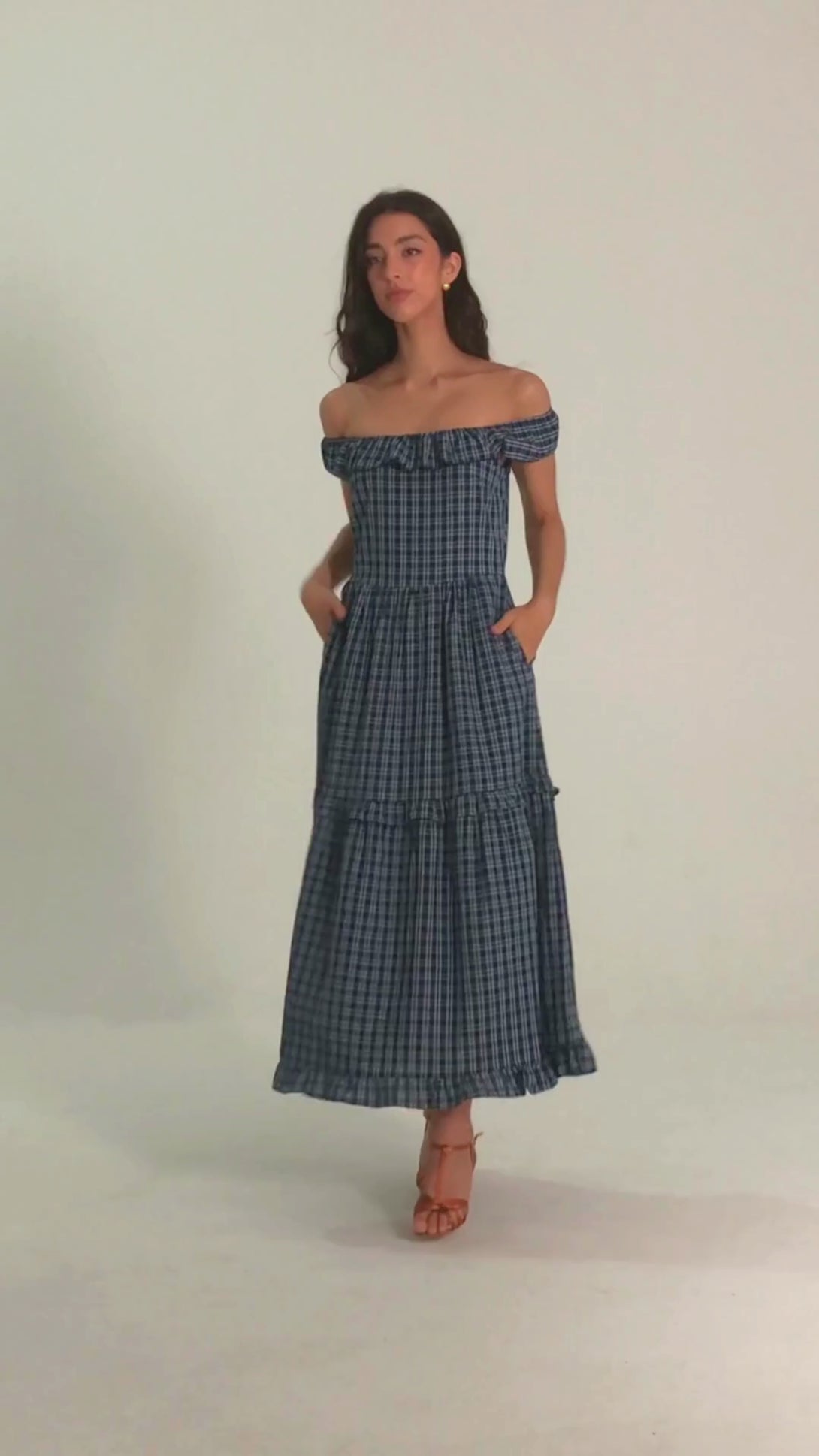 Woman wearing a blue off-shoulder gingham maxi dress with ruffle trim, perfect for summer getaways or outdoor brunches.
