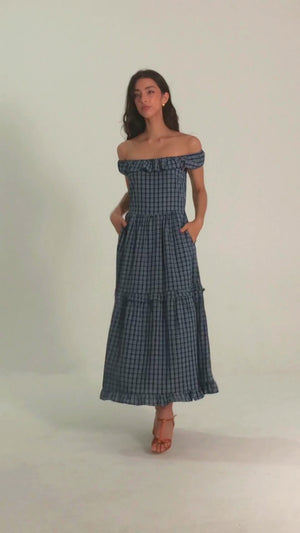 Woman wearing a blue off-shoulder gingham maxi dress with ruffle trim, perfect for summer getaways or outdoor brunches.