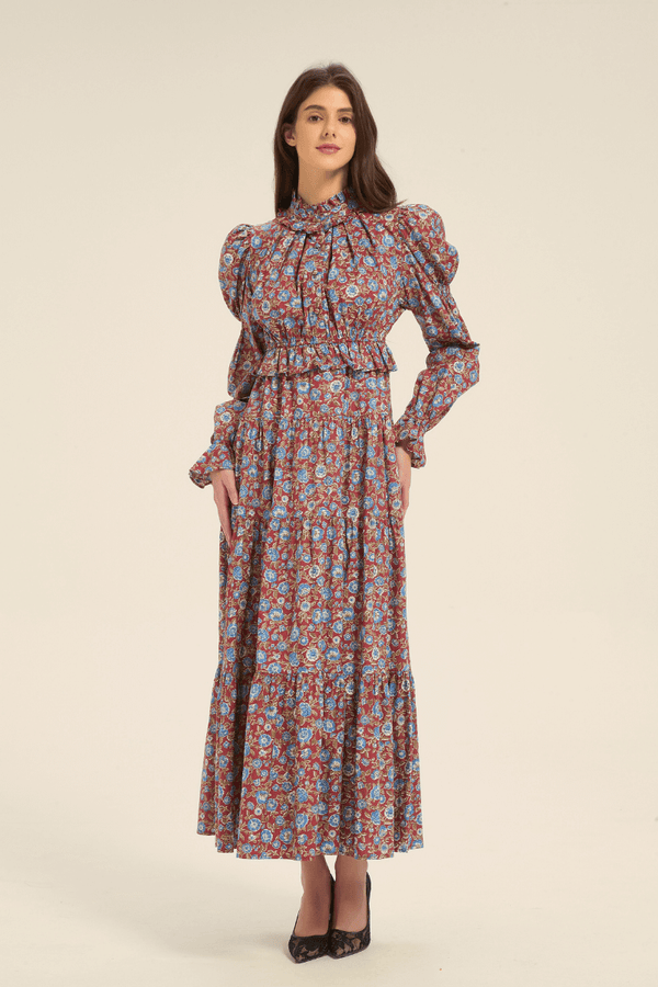 Full-length front view of a red floral print maxi dress with blue flowers, high neckline, and flowing tiered skirt.