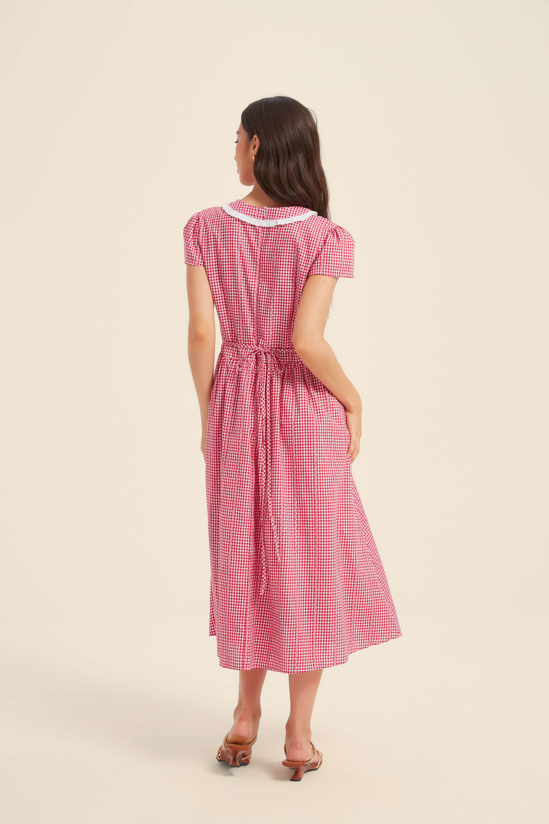 Back view of a red gingham midi dress with short sleeves, a white scalloped collar, and adjustable waist tie.