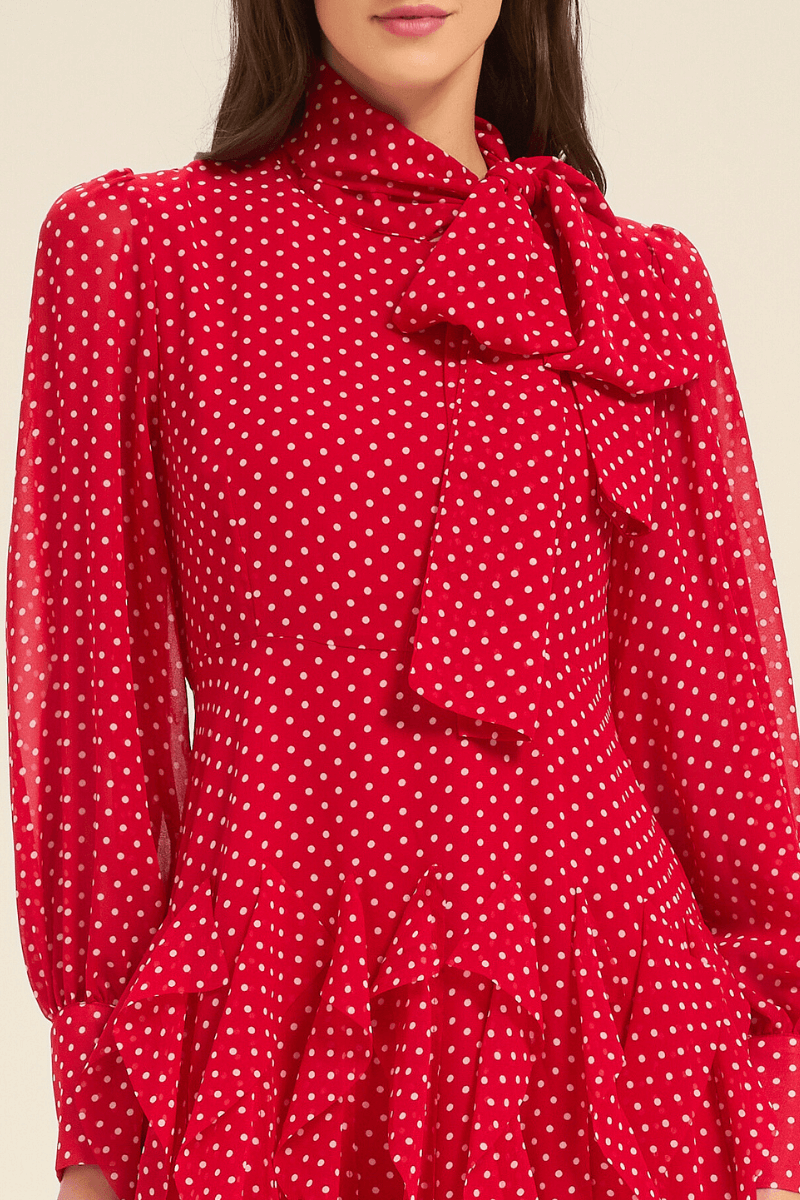 Close-up of red polka dot dress featuring bow tie neckline and sheer long sleeves.
