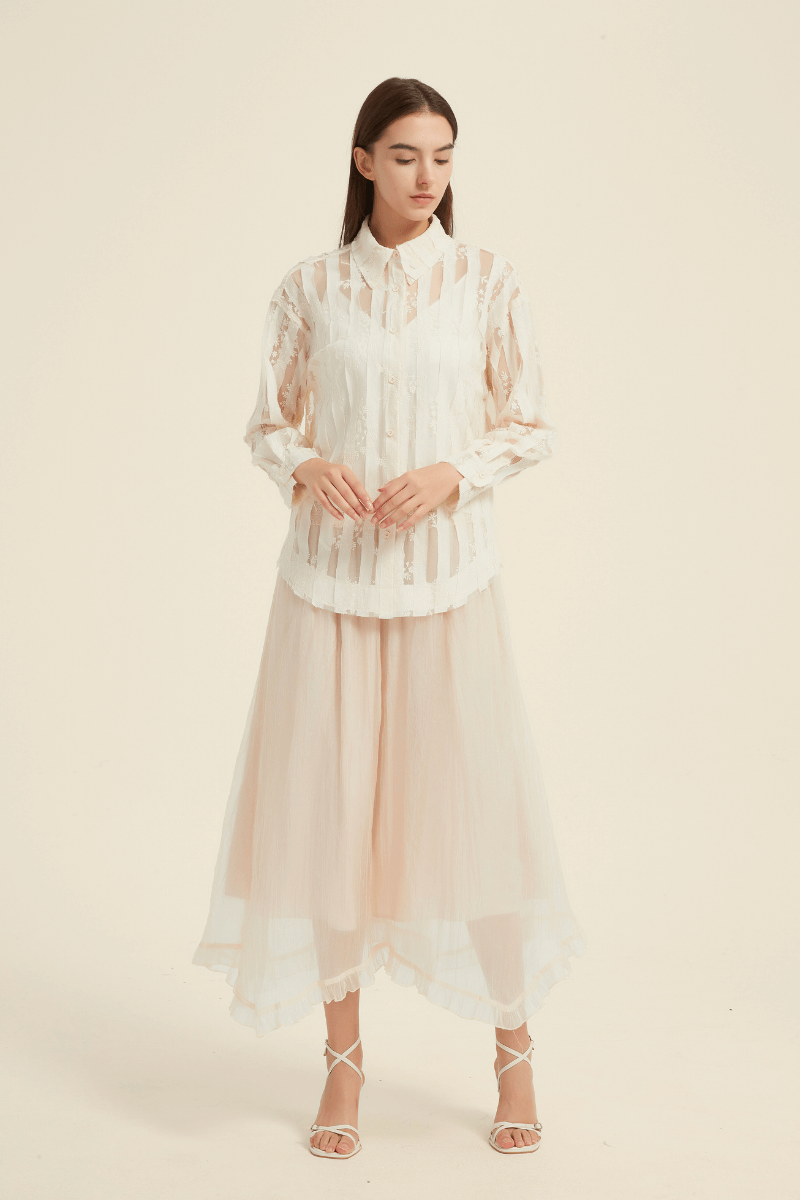 Model wearing a cream sheer lace button-up blouse paired with a flowy blush pink asymmetric tulle midi skirt, styled with white strappy heels.