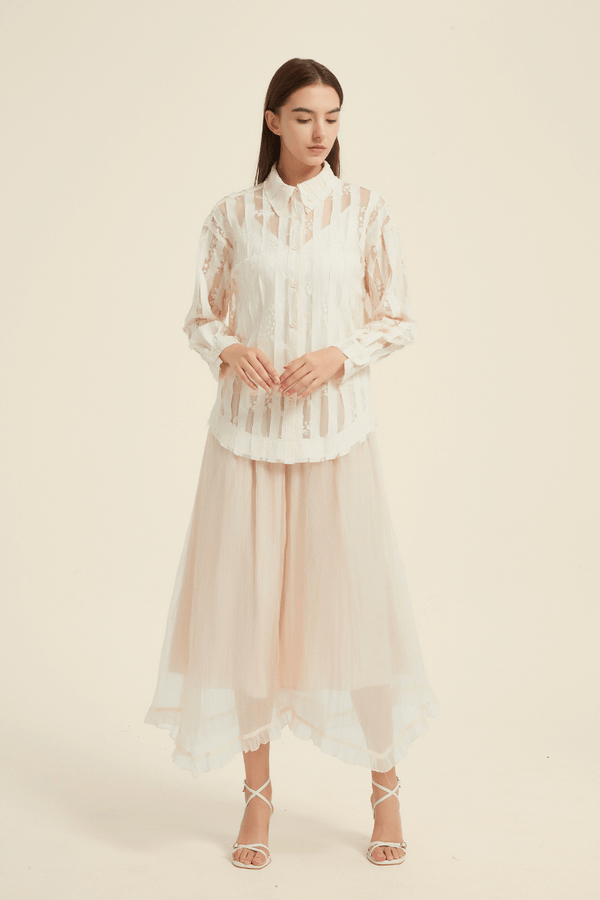 Model wearing a cream sheer lace button-up blouse paired with a flowy blush pink asymmetric tulle midi skirt, styled with white strappy heels.