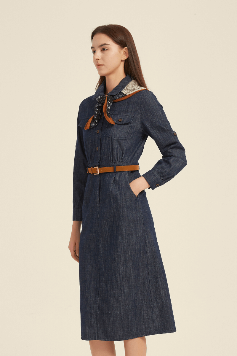 Side view of a denim midi shirt dress featuring chest flap pockets, long sleeves, a brown waist belt, and a printed scarf tied at the collar for a western-inspired look.