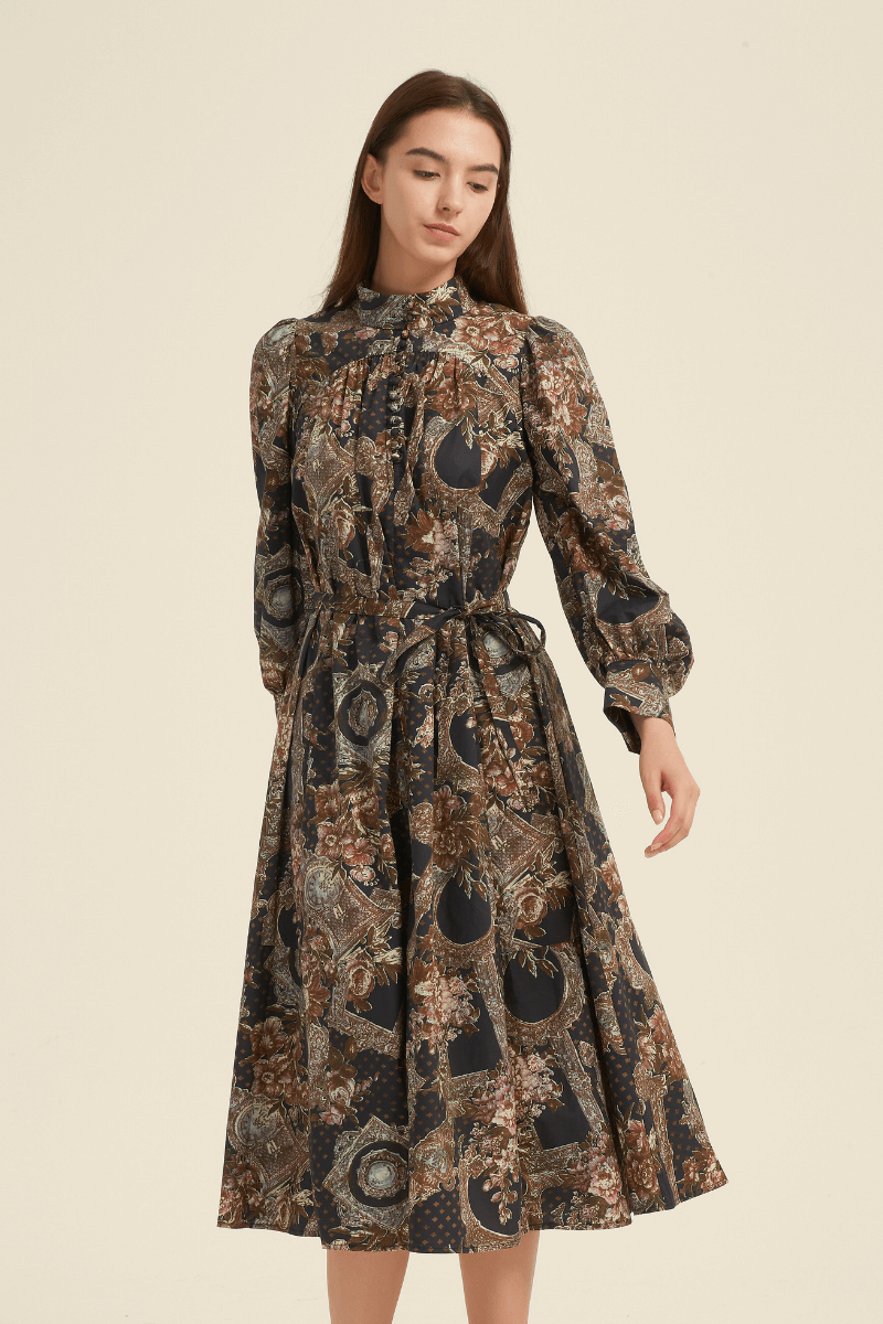 Front view of a vintage baroque-print midi dress featuring long puff sleeves, a high neckline with button details, a waist tie, and an A-line skirt in ornate floral and frame patterns of brown, gold, and navy.