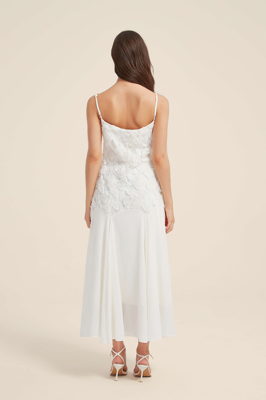 Back view of a white maxi dress with delicate shoulder straps, 3D floral bodice, and flowing chiffon skirt.
