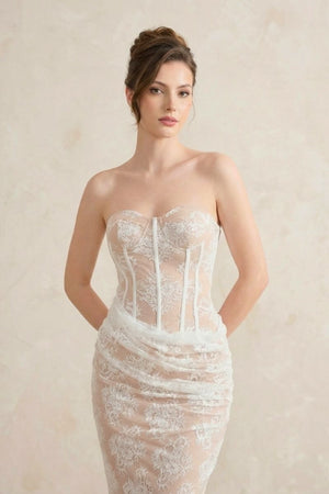 A close-up of the strapless white lace corset dress, highlighting the structured boning, sweetheart neckline, and sheer floral lace.