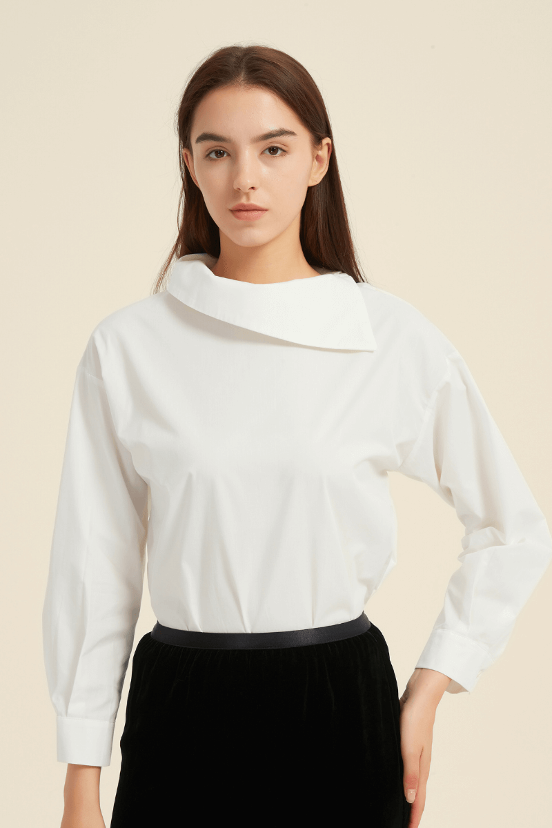 Close-up front view of a woman wearing a white long-sleeve blouse with an asymmetric folded collar, paired with a black waistband skirt.