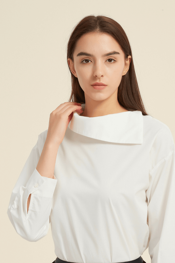 Close-up of a woman wearing a white long-sleeve blouse featuring an asymmetric folded collar and buttoned cuffs, made from smooth lightweight fabric.