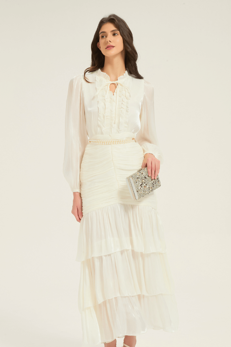 Model wearing the white ruffle tiered midi dress with pearl belt, styled with a silver clutch for an evening-ready look.