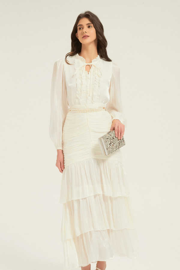 Model wearing the white ruffle tiered midi dress with pearl belt, styled with a silver clutch for an evening-ready look.
