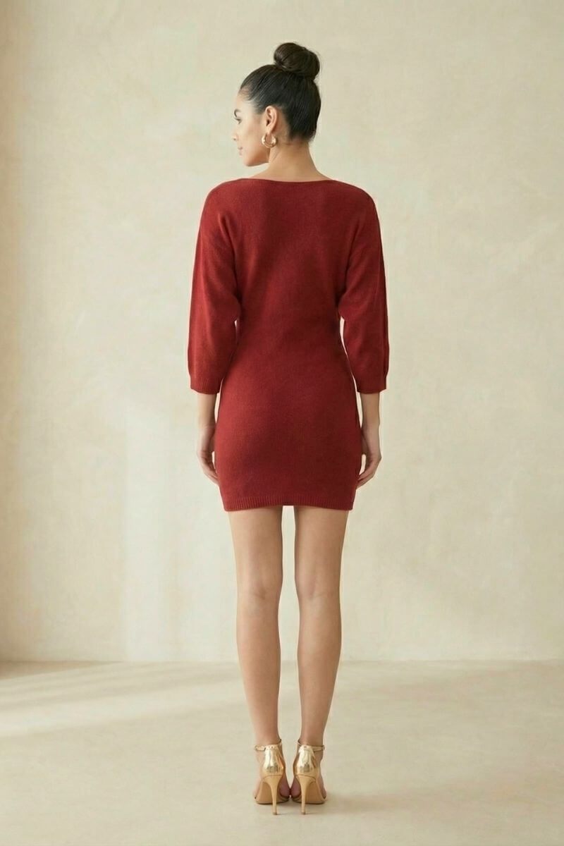 A woman faces away from the camera wearing a wine-red knit mini dress with three-quarter sleeves, shown in a clean studio setting to highlight the simple back view and fitted silhouette.