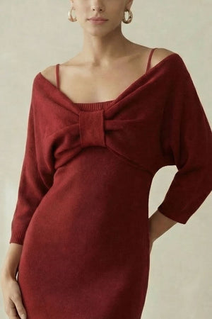 A close-up of a woman in a wine-red knit mini dress featuring an off-shoulder neckline, thin straps, and a centered bow detail, photographed in a soft neutral studio.