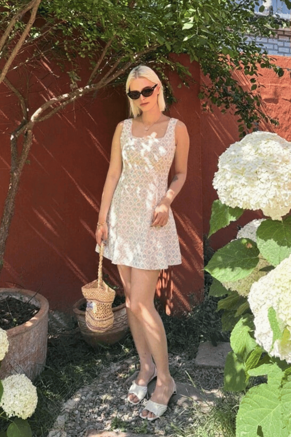 Woman wearing a sleeveless blue floral mini dress with square neckline in a summer garden setting