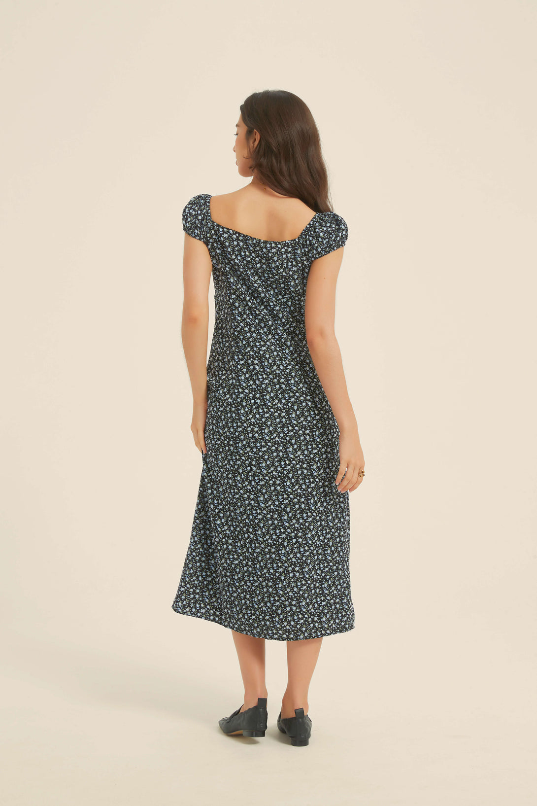 Back view of a woman wearing a black floral midi dress with puff sleeves and a square neckline