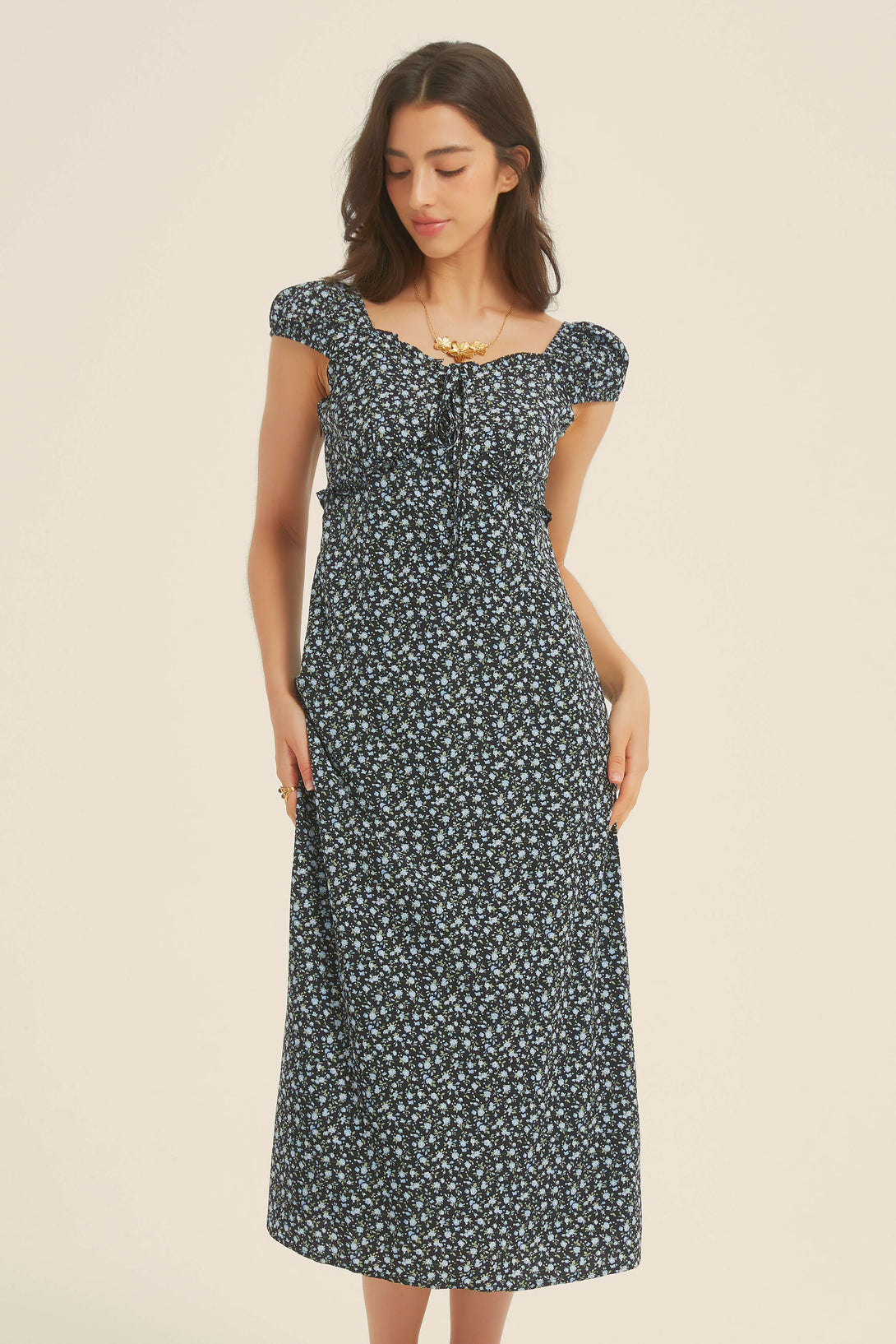 Front view of a woman wearing a black floral midi dress with puff sleeves, ruched bust, and sweetheart neckline