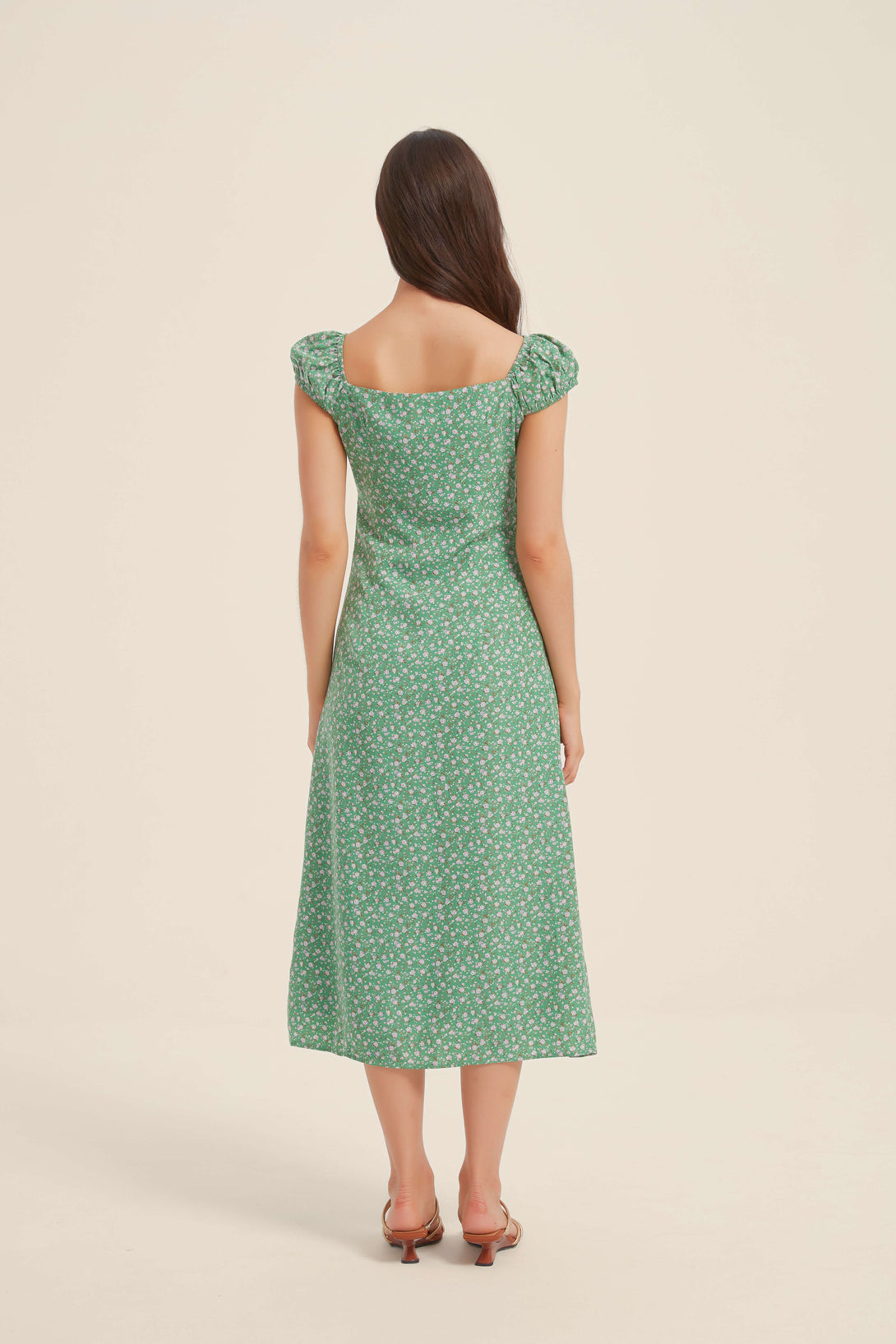 Back view of a woman wearing a green floral midi dress with puff sleeves and a softly fitted waistline
