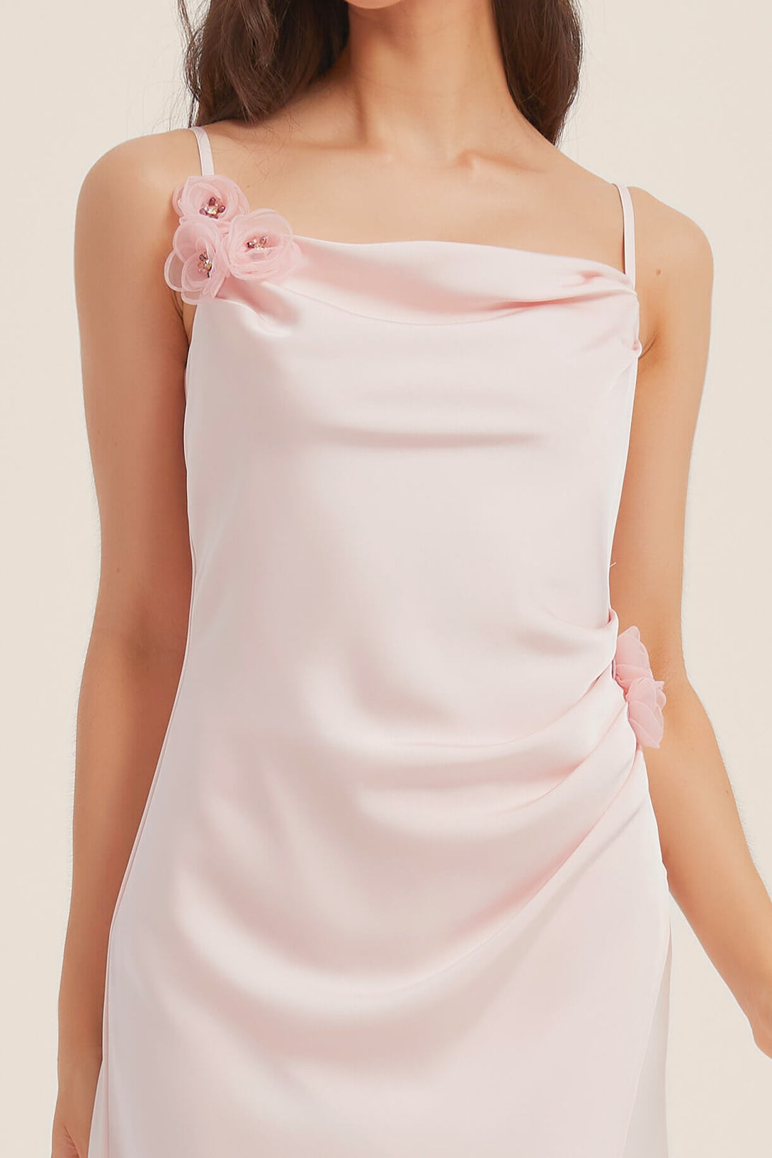 Close-up of pink satin midi dress showing floral rosette details at the shoulder and waist with soft draping neckline