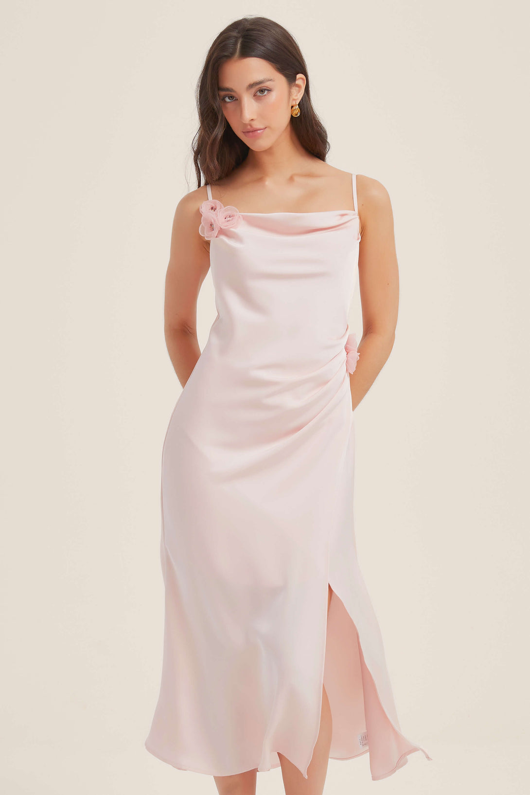 Model wearing a soft pink satin midi dress with floral appliqués, cowl neckline, and side slit — elegant and romantic look.