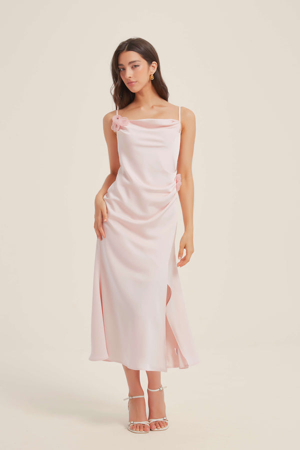 Full front view of a woman wearing a pink satin midi dress with cowl neckline, side slit, and delicate floral details