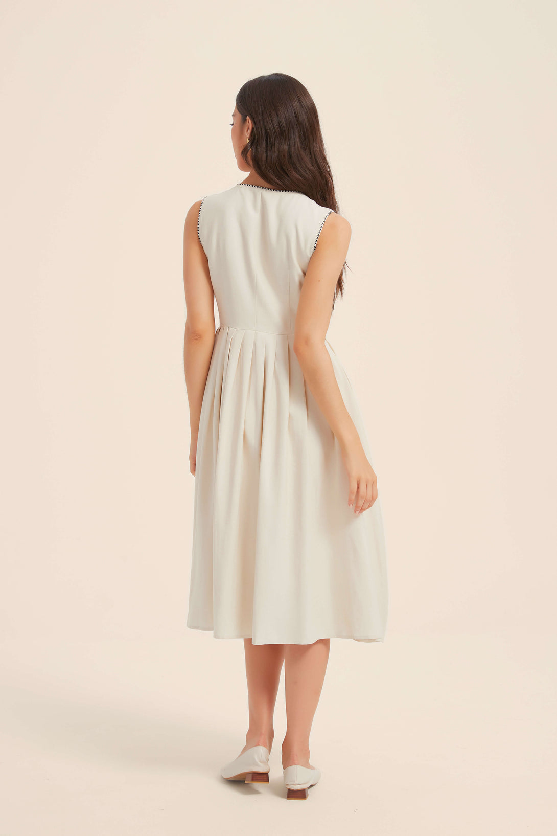 Back view of a sleeveless white midi dress featuring a fitted bodice, gathered waist, and soft pleats for a vintage-inspired silhouette.