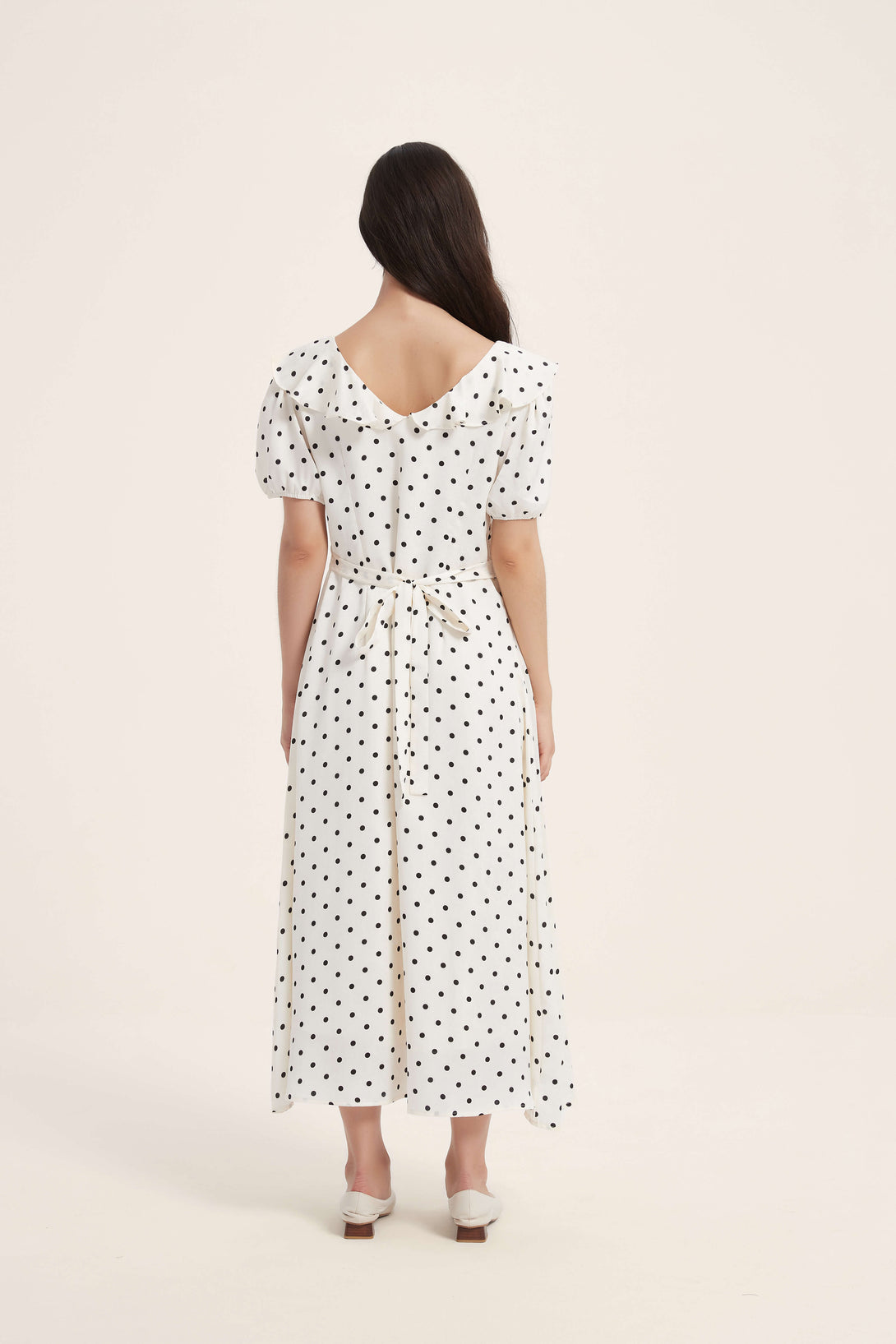 Full back view of a white polka dot midi dress with puff sleeves, ruffled collar, and waist tie detail