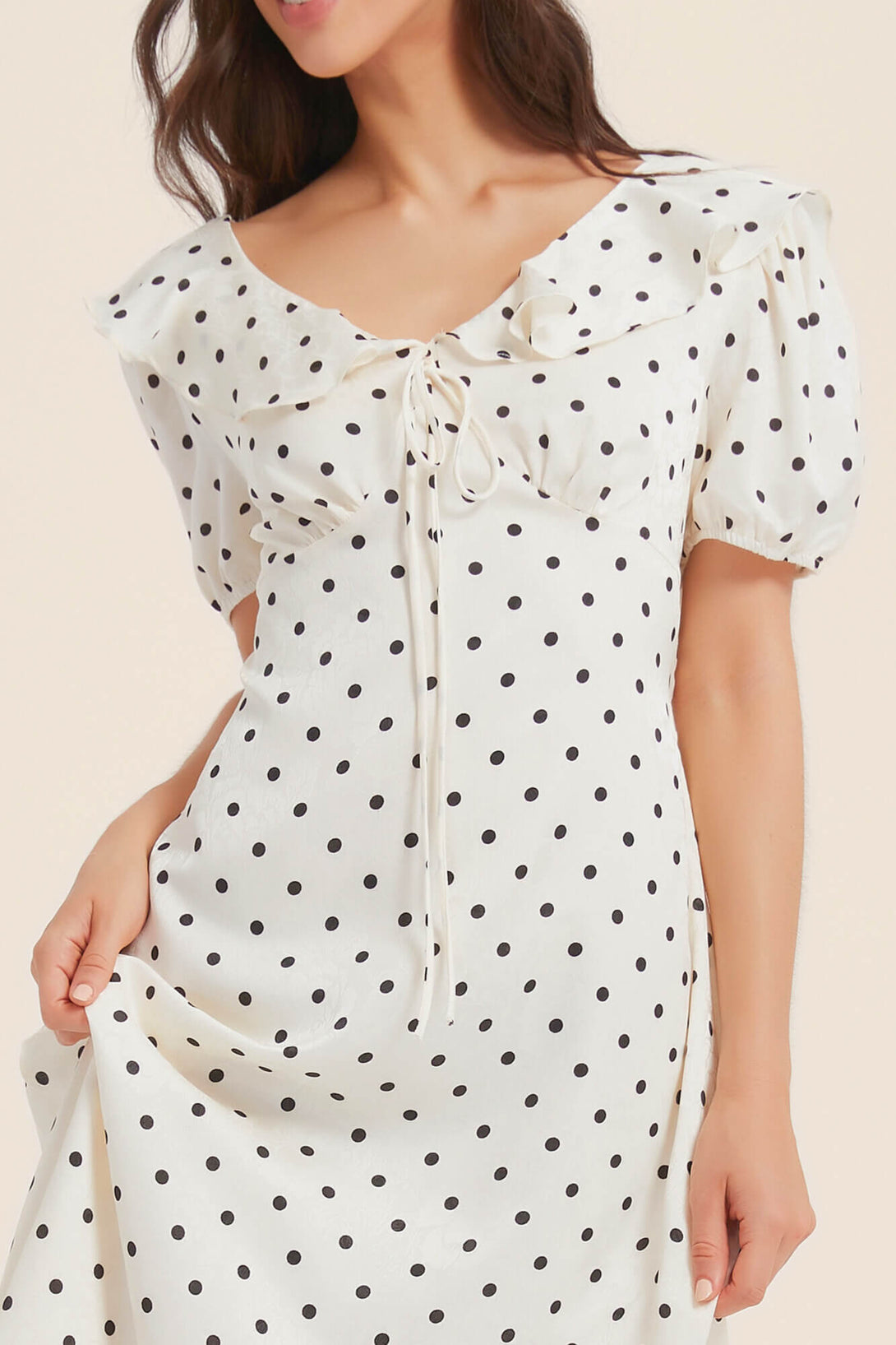 Close-up of a white puff-sleeve midi dress with black polka dots, showing ruffled neckline and front tie detail