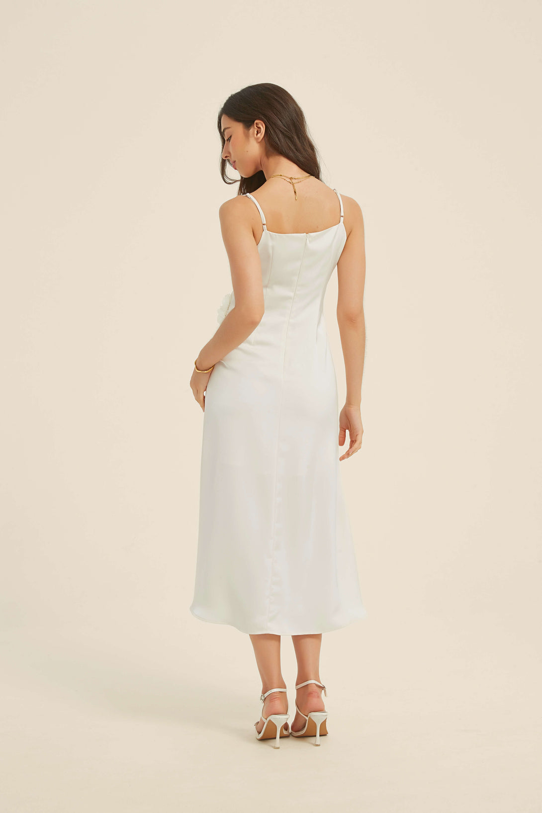 Back view of a white satin midi dress with thin shoulder straps and an invisible center-back zipper, styled with strappy heels and soft curls