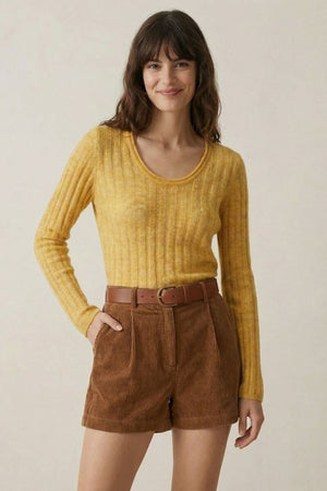 A woman wearing a yellow ribbed scoop-neck sweater paired with high-waisted brown corduroy shorts and a tan belt, standing against a neutral background.